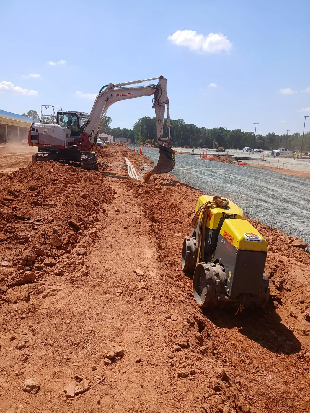 Excavator opening a utility trench next to a trench roller ready for compaction